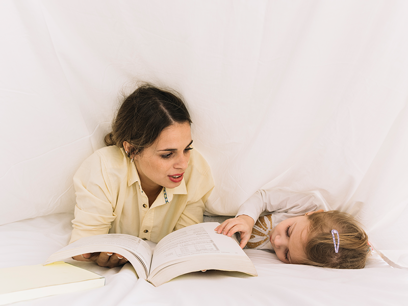 Mãe lê uma história para a sua filha dormir na cama