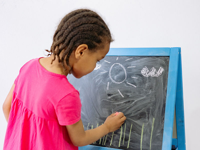 menina com blusa rosa desenhando em uma louza com giz
