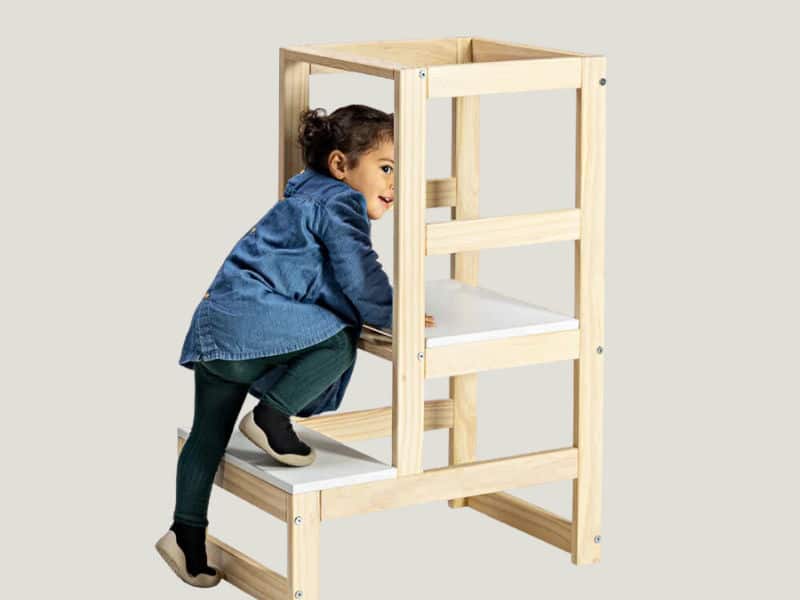 criança feliz subindo em uma torre montessoriana para organizar o quarto