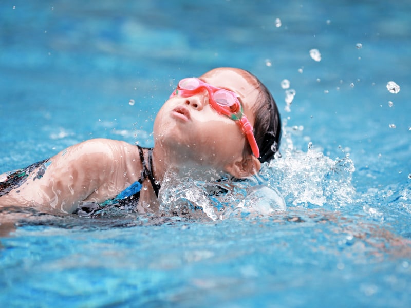 criança autista com um óculos vermelho nadando na piscina 