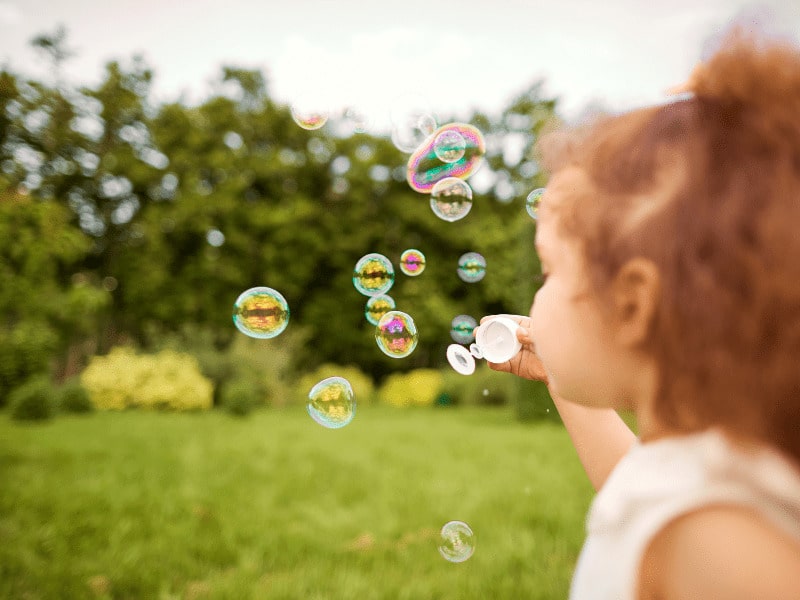 Menina autista com cabelo enrolado fazendo bolhas de sabão em um campo aberto 