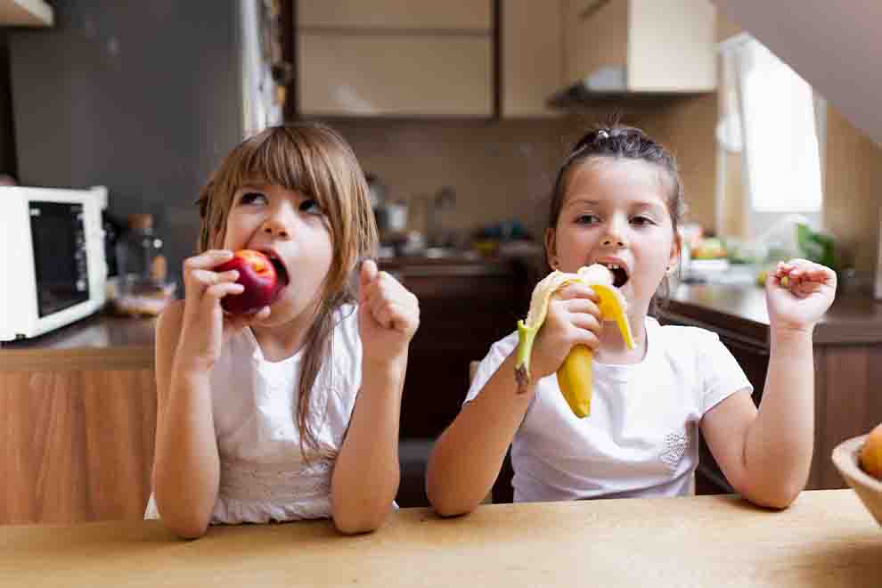 duas crianças degustando frutas diferentes em uma cozinha 