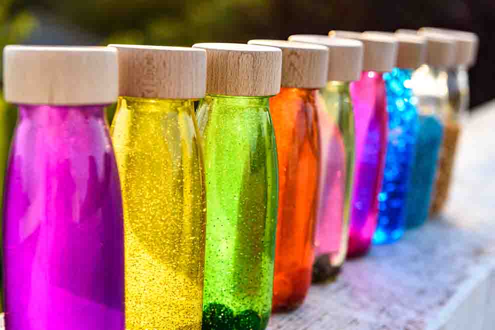 várias garrafas sensoriais com águas coloridas ao ar livre 