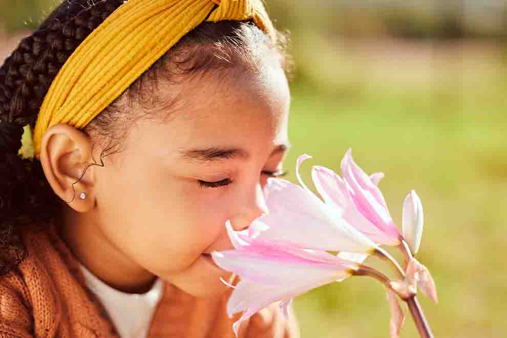 criança cheirando uma flor em um campo