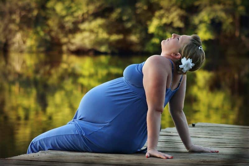 Mulher grávida sentada com o corpo inclinada para traz apoiando-se com as mãos