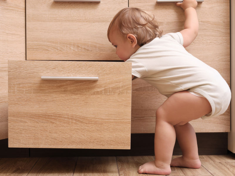 criança com cerca de 1 a 3 anos abrindo a gaveta do armário da cozinha