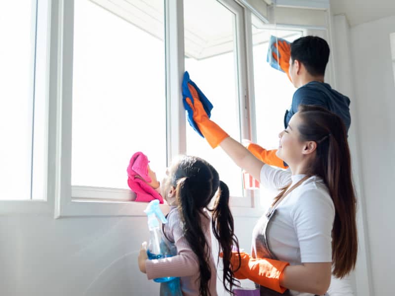 mãe, pai e filha limpando o vidro da janela com luvas e paninho 