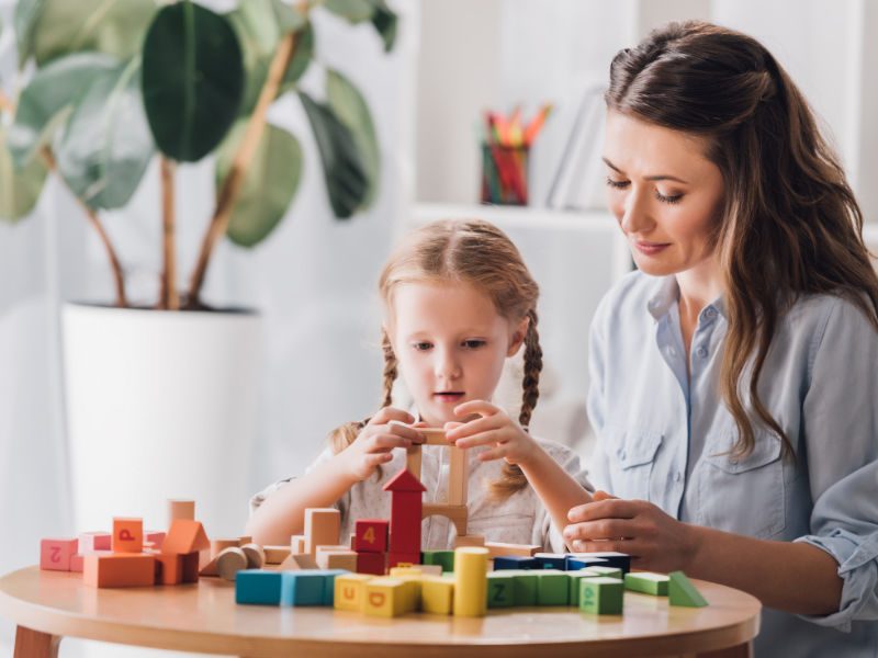 mãe ao lado de uma filha com 5 ou 6 anos brincando de blocos de montar para desenvolver o lado cognitivo