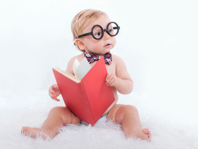 bebê com um óculos segurando um livro na mão