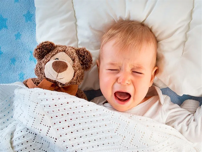 Criança chorando na cama com um ursinho de pelúcia marrom ao lado