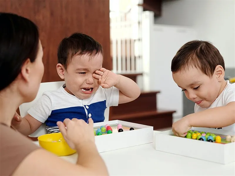 Menino chorando na mesa na frente do irmãozinho e da mãe