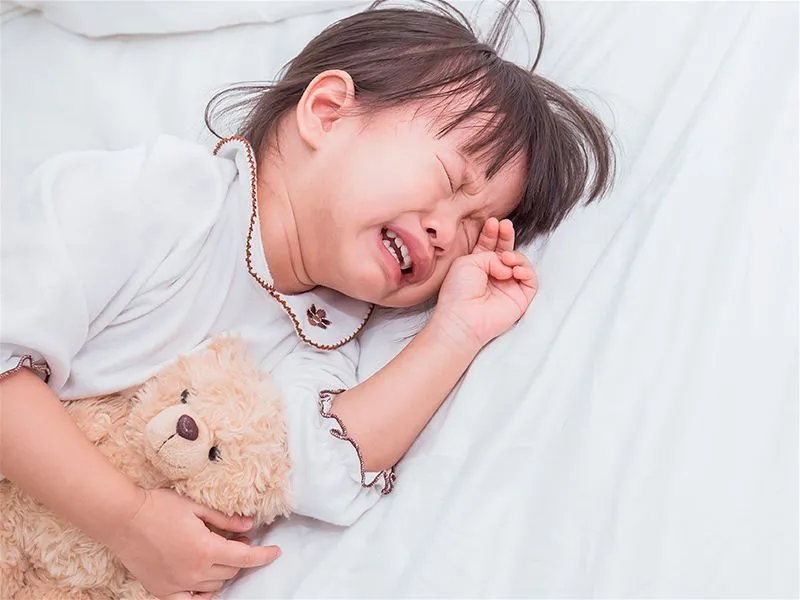 Criança chorando na cama abraçada com um ursinho