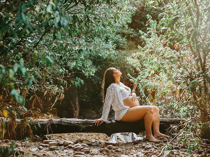 Mulher grávida sentada em meio de floresta.