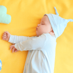 Bebê dormindo pacificamente em cima de um cobertor amarelo com bichinhos de pelúcia