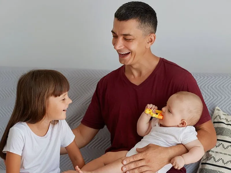 pai, filha e bebê sorrindo juntos enquanto o bebê brinca com um mordedor