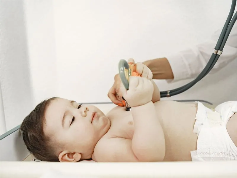 bebê segura brinquedo enquanto médico o examina com estetoscópio