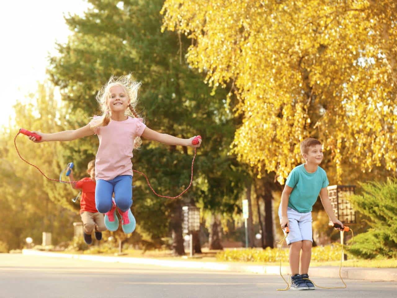uma menina e dois menino pulando corda felizes