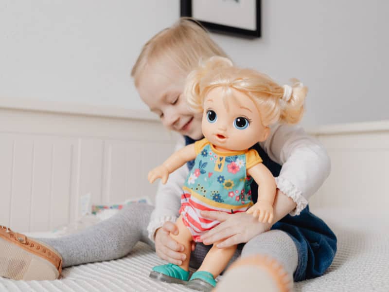 menina feliz brincando com uma boneca que ganho de Natal em cima da cama