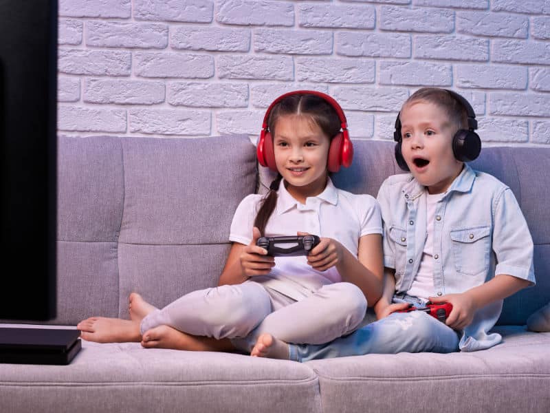 uma menina e um menino jogando vídeo game no sofá