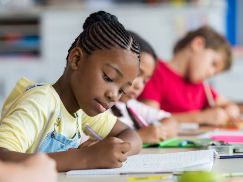 menina com uma blusa amarela escrevendo no caderno em uma sala de aula
