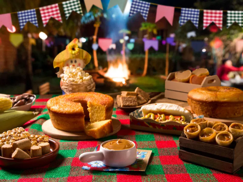 mesa com quitutes de festa julina: bolo, paçoca, canudo e mais