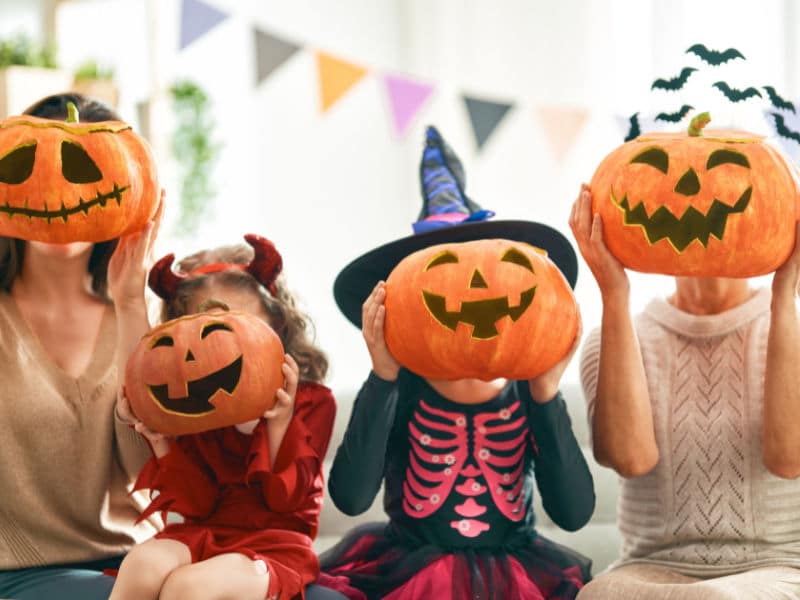 quatro crianças sentadas em fileira com uma abóbora de hallowen no rosto