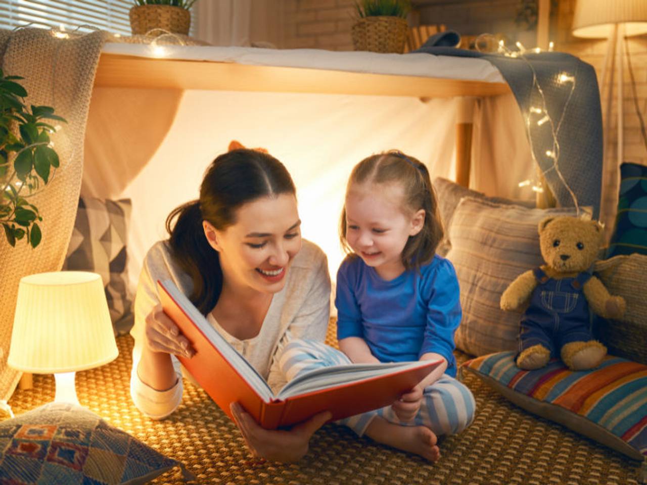 mãe feliz lendo para a filha em uma cabaninha