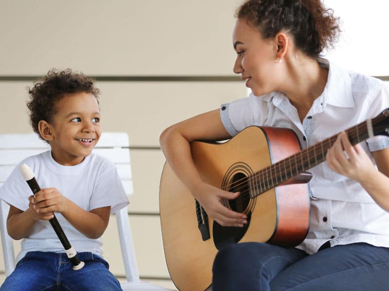 mulher tocando violão ao lado de um menino tocando flauta