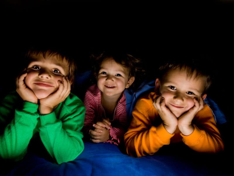 dois meninos e uma menina felizes com a mão no rosto e deitados em uma cabana