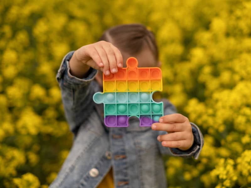 menino segurando uma peça de quebra-cabeça com as cores do autismo