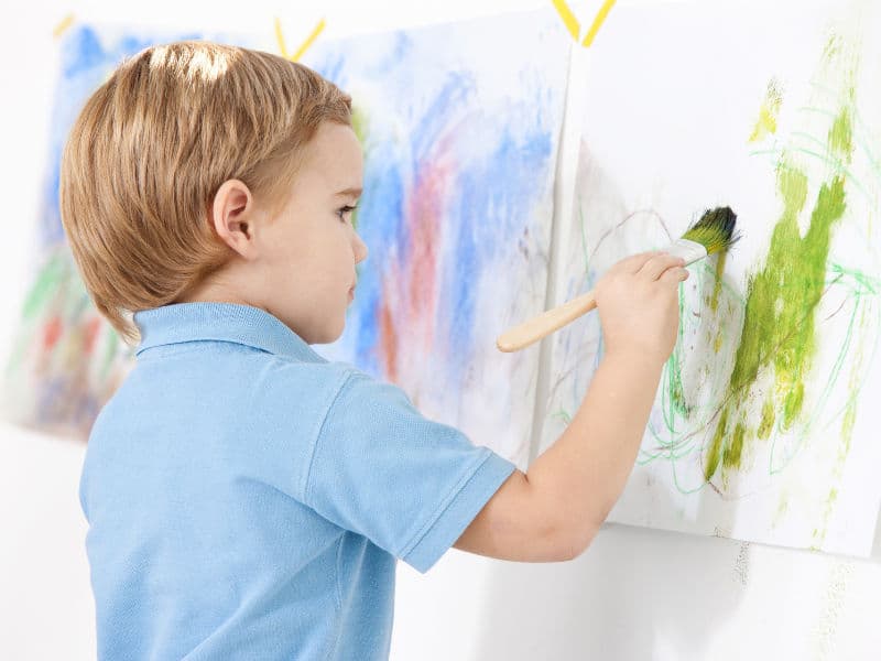 menino pintando um quadro com pincel e fazendo Atividades de arte para desenvolver habilidades motoras finas