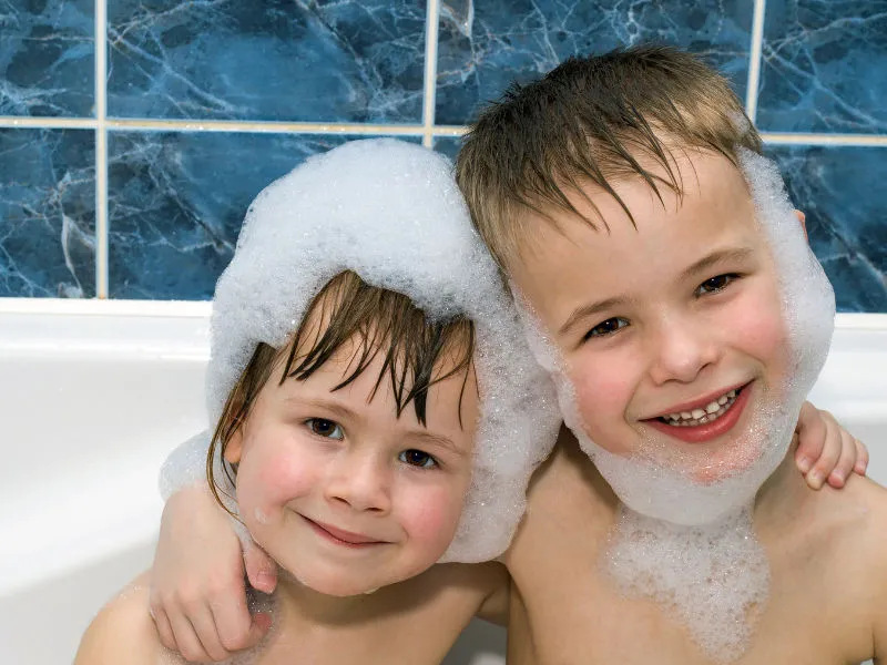 dois irmãos pequenos na banheira com várias espumas 