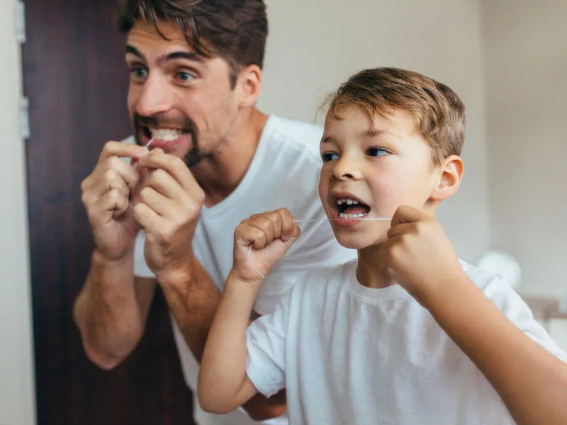 pai e filho passando fio dental nos dentes 