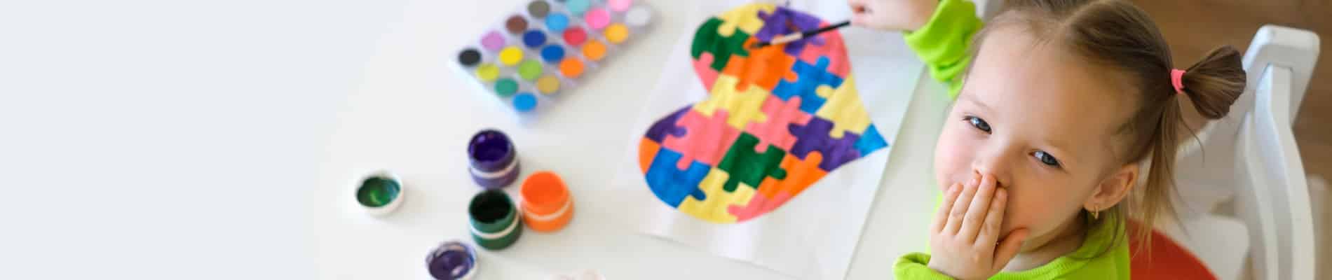 criança pintando um coração com as cores e os símbolos do autismo
