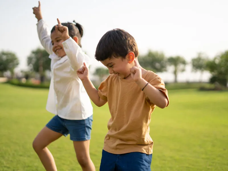 um menino e uma menina dançando felizes em um gramado verde