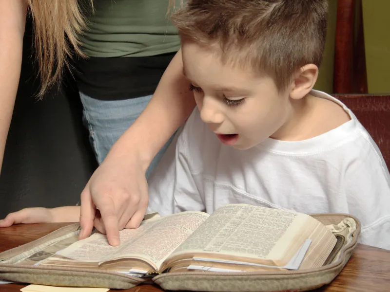 menino na mesa lendo livro em voz alta para trabalhar as vogais