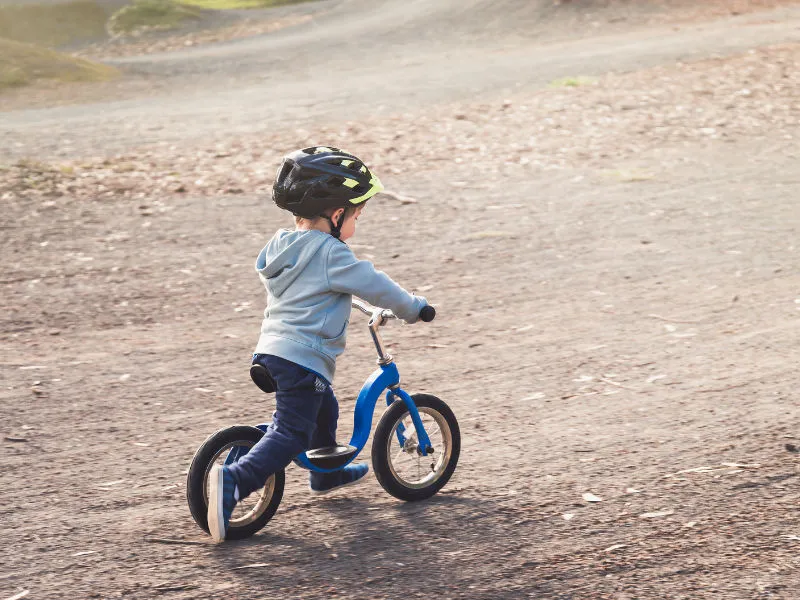 criança de três anos andando em uma mini bicicleta com capacete
