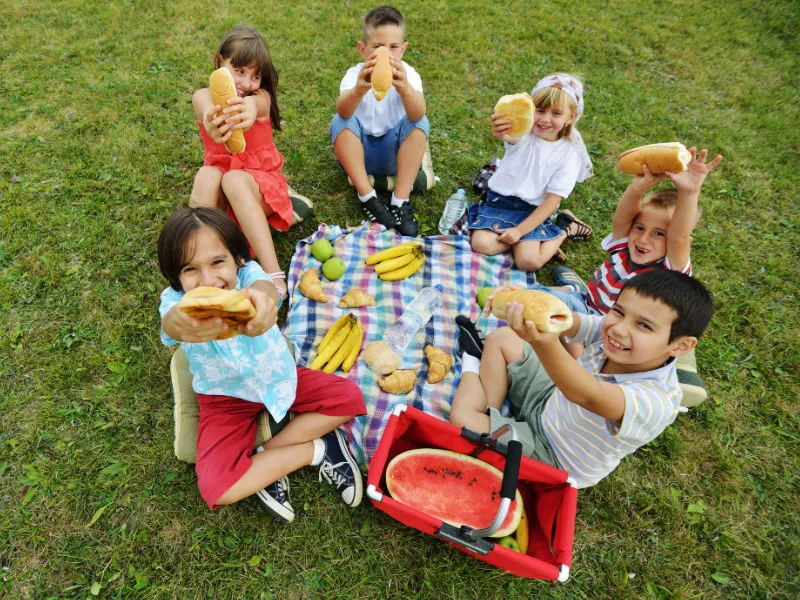 crianças pequenas em um piquenique comendo pão baguete