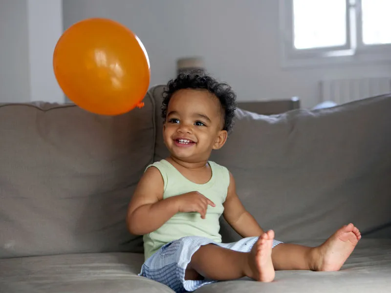 bebê no sofá brincando de volei com um balão