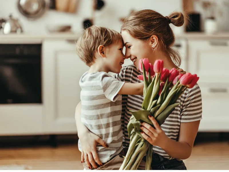 mãe abraçada com seu filho de três anos no colo segurando um buque de tulipas