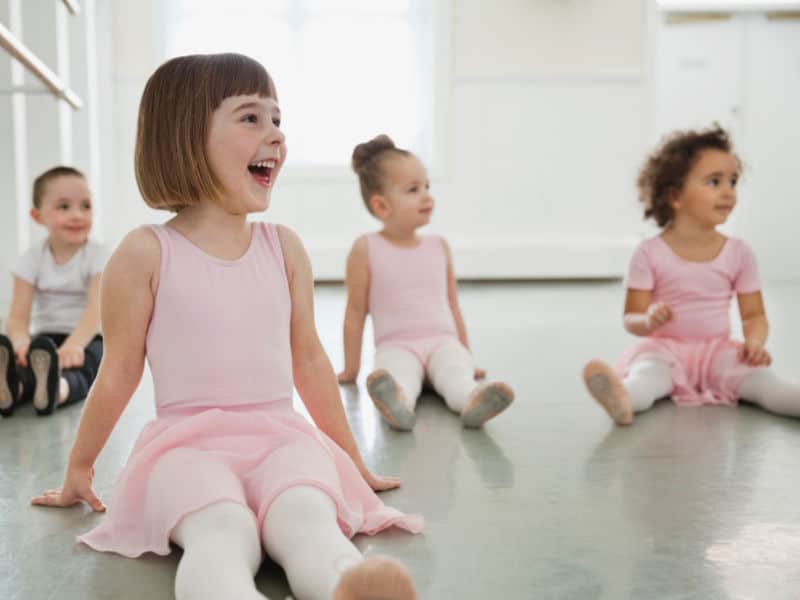 crianças sentadas em uma sala de dança com roupinhas de balé