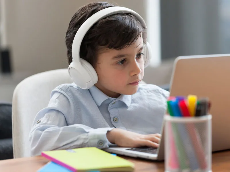 menino de 7 anos com fone de ouvido mexendo no computador