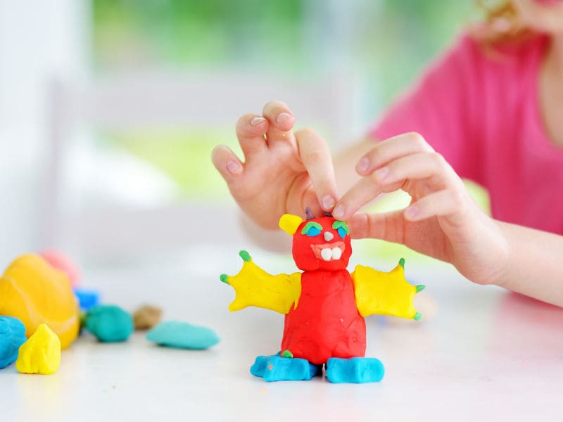 menina com mais de dois anos brincando de massinha de modela na mesa