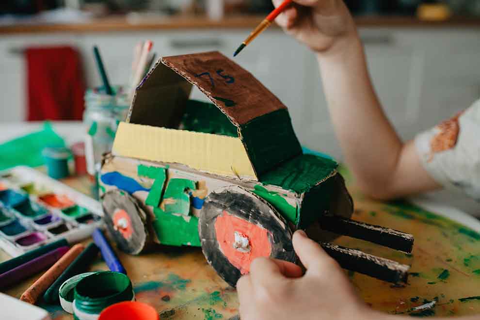 Criança pintando carro de papelão colorido