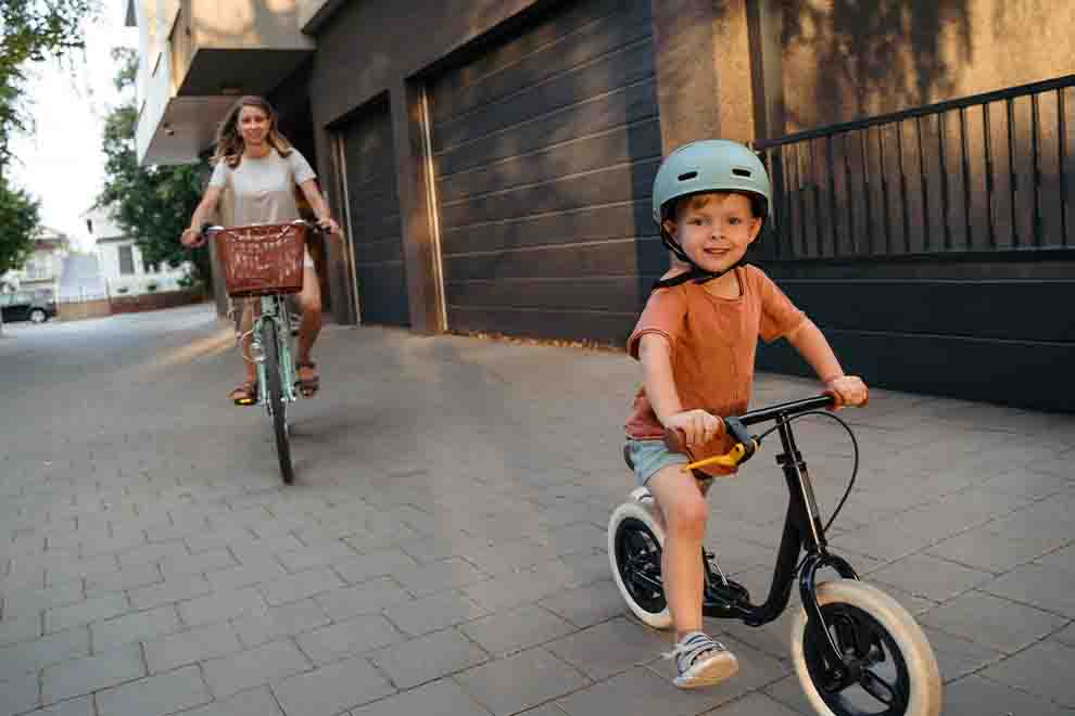 Criança pedalando bicicleta com capacete e mulher atrás