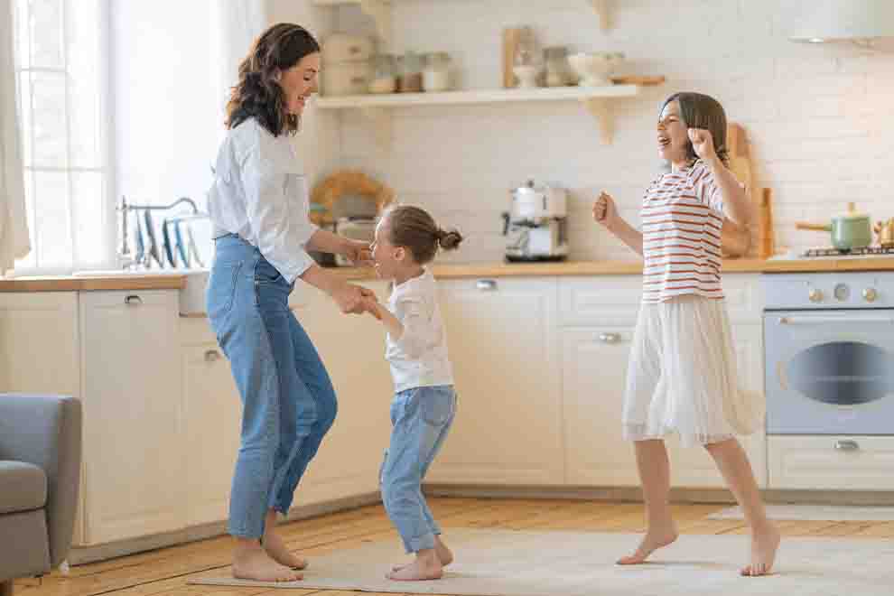 Mãe e filhas dançando felizes na cozinha