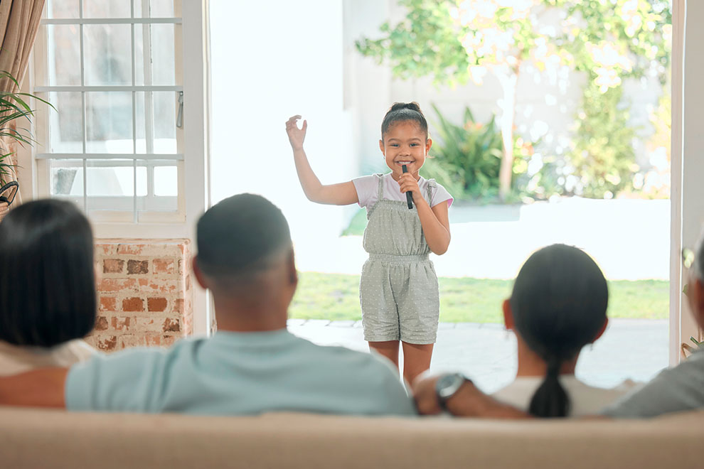 Menina se apresentando com microfone para a família.