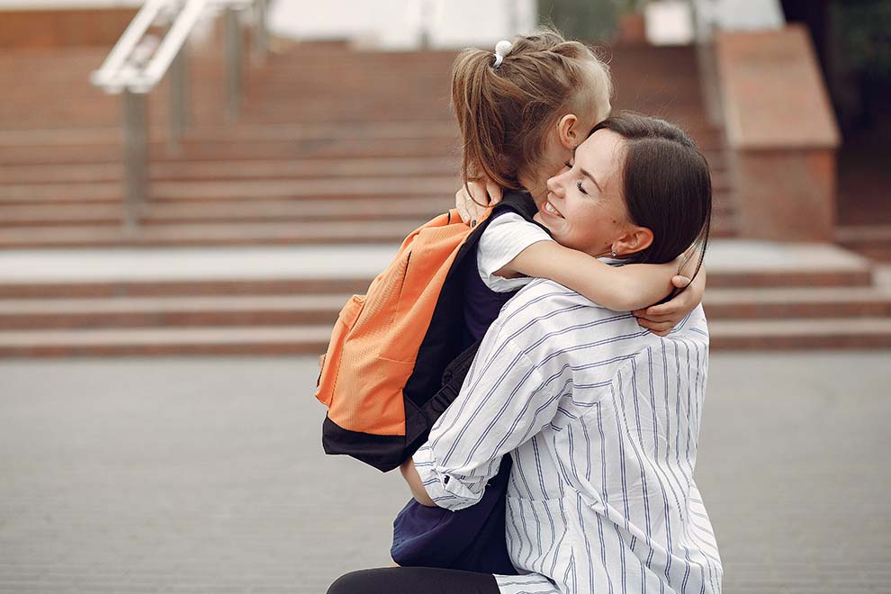 Mãe abraçando filha com mochila